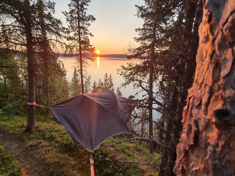 Hammock suspended between trees overlooking a lake at sunset.