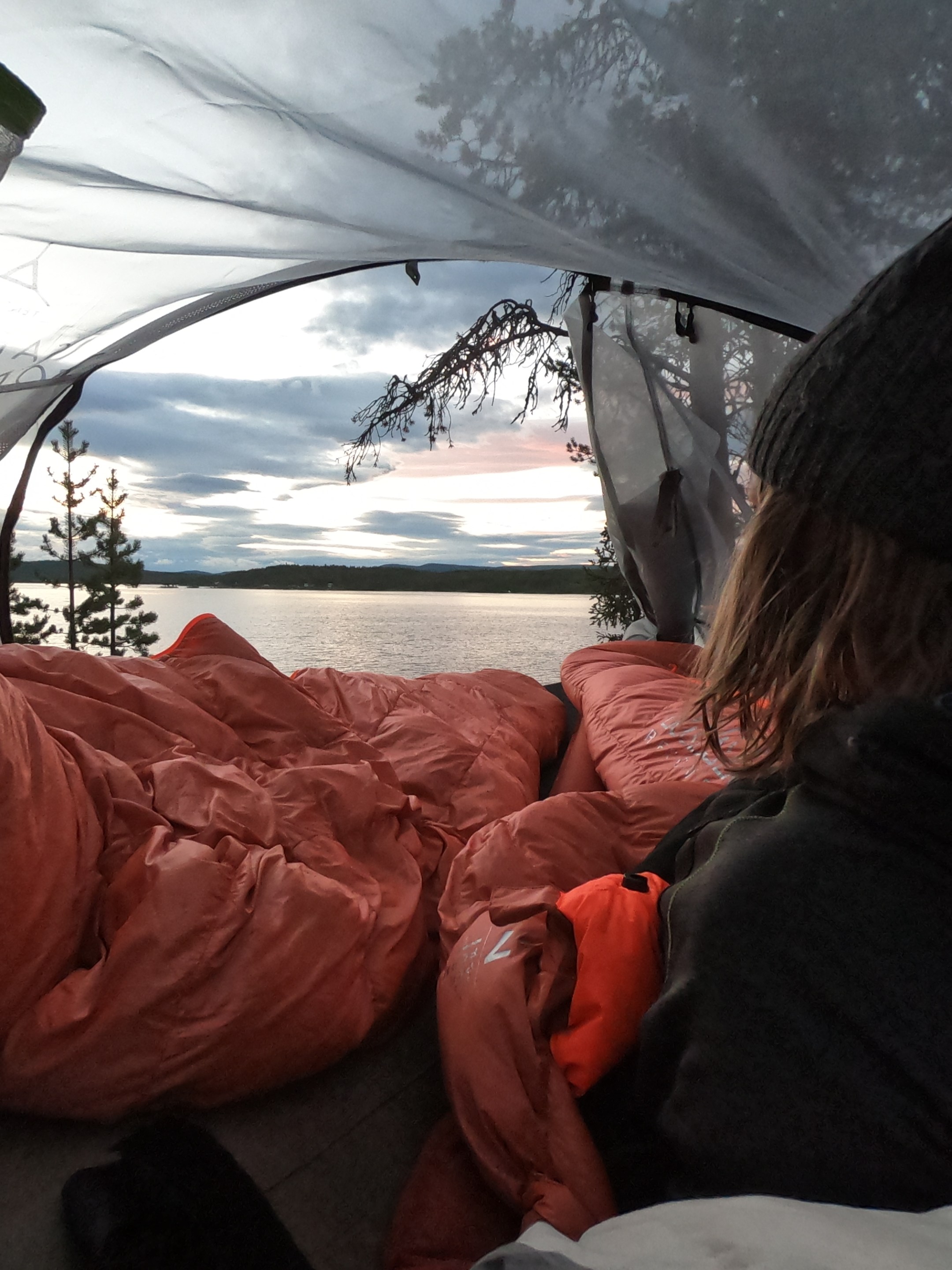 Person in tent looking at lake and trees during sunset.