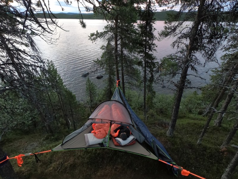 Suspended tent among trees with view of a lake at dusk.