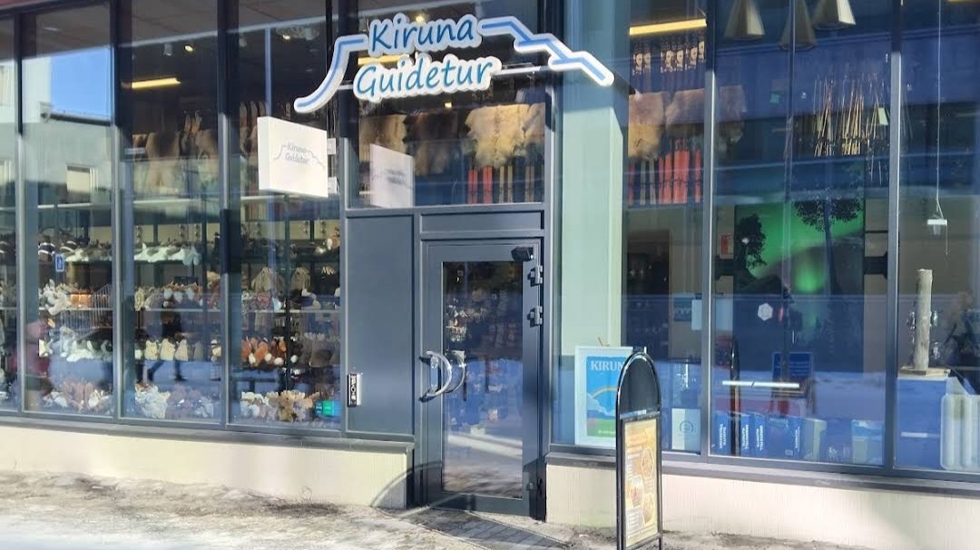 Storefront with 'Kiruna Guidetur' sign, glass windows, and a small entrance door.