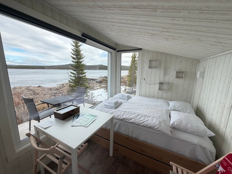 Cozy cabin bedroom with a large window view of a lake and forest.