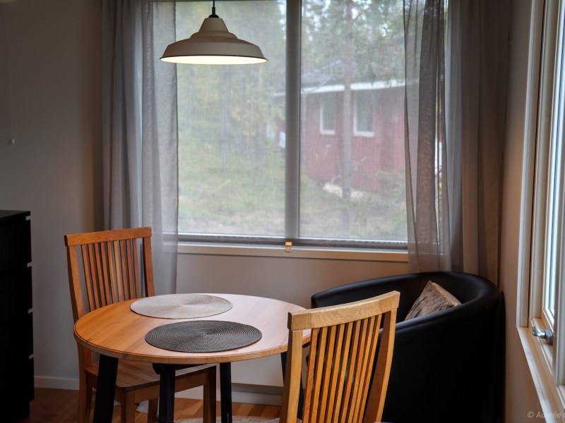 Cozy dining area with round table, wooden chairs, armchair, and window with sheer curtains.