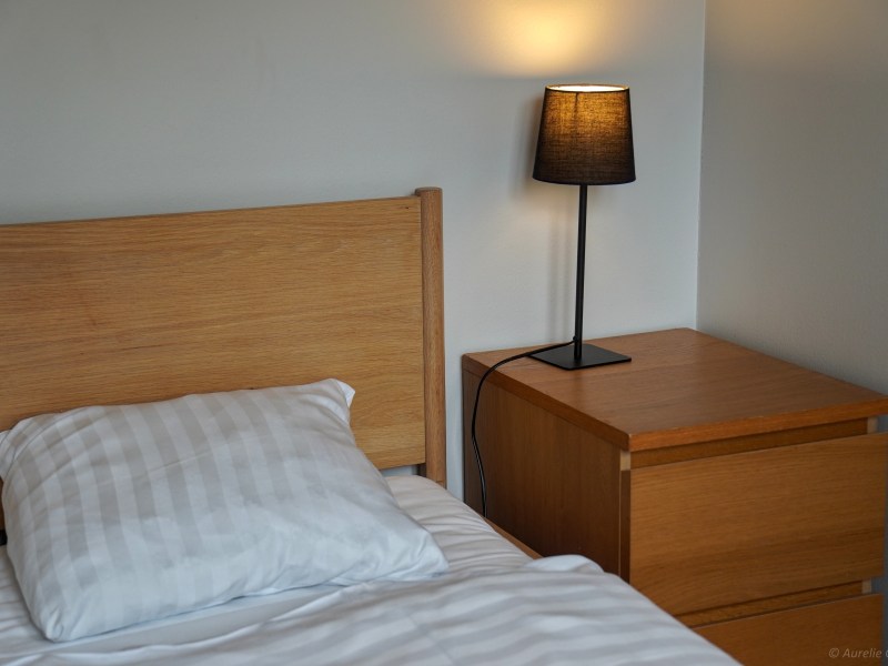 Bedroom with wooden bed, striped pillow, and bedside table with lamp.