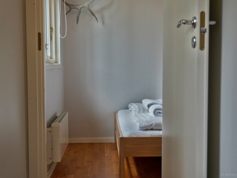 View of a minimal bedroom with wooden bed, folded towels, and antlers on the wall.